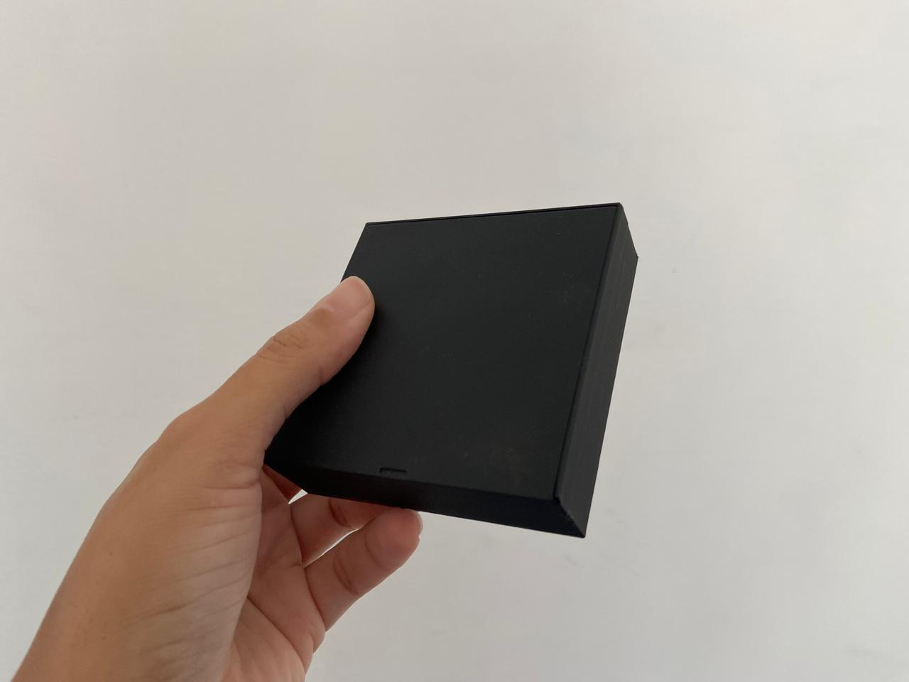 Caixa preta para sachês de chá impressa em 3D, com a tampa fechada, na palma da mão.