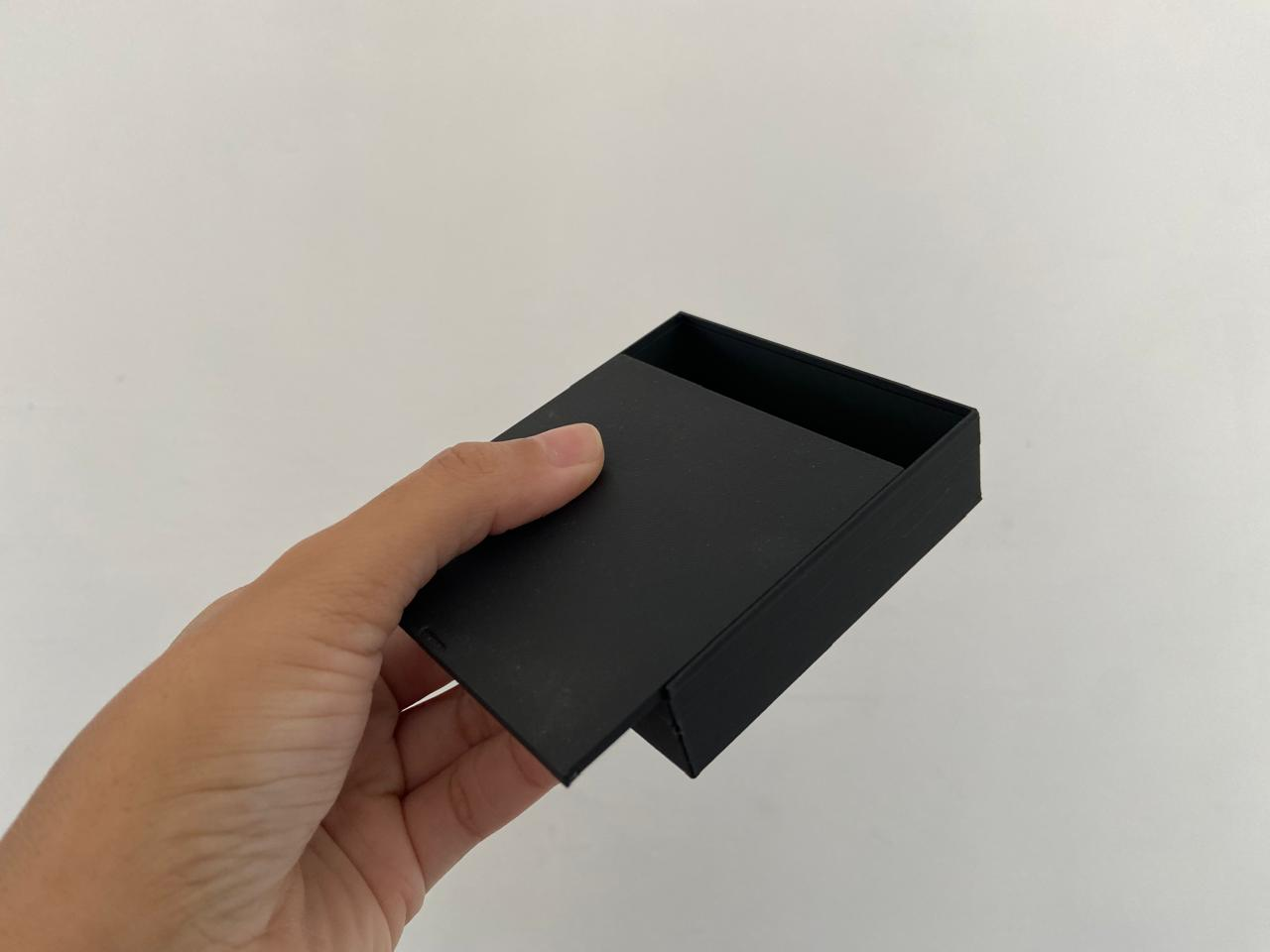 Caixa preta impressa em 3D vista de lado, com a tampa deslizante parcialmente aberta.